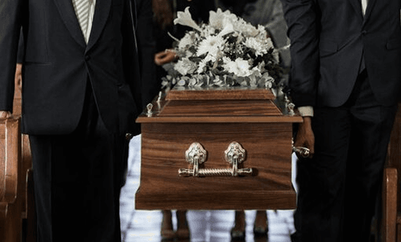 Pallbearers carrying a wooden casket topped with white flowers