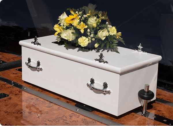 Small white casket topped with yellow and cream flowers